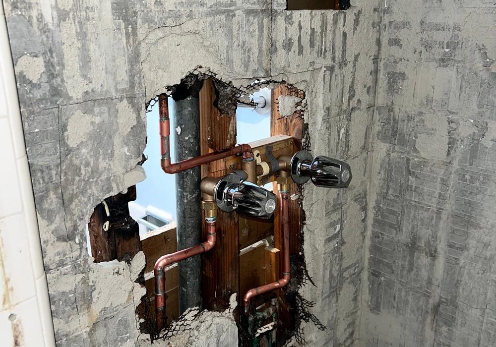 Shower valve and copper supply lines exposed through an opening cut in a tiled bathroom wall