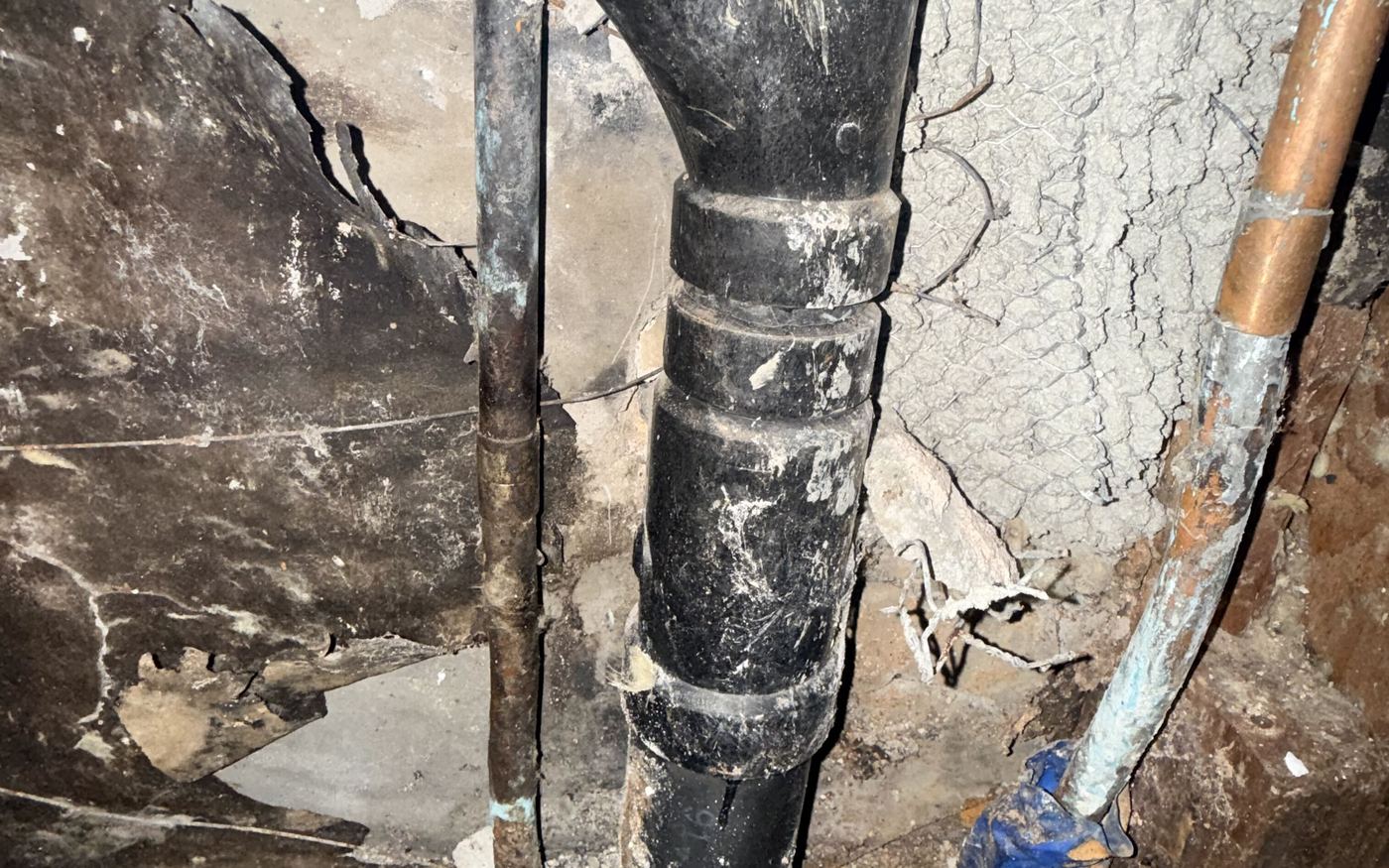 New black ABS drain piping with couplings running under floor joists in a crawl space