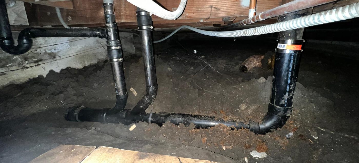 New black ABS drain and vent piping running under floor joists across a crawl space