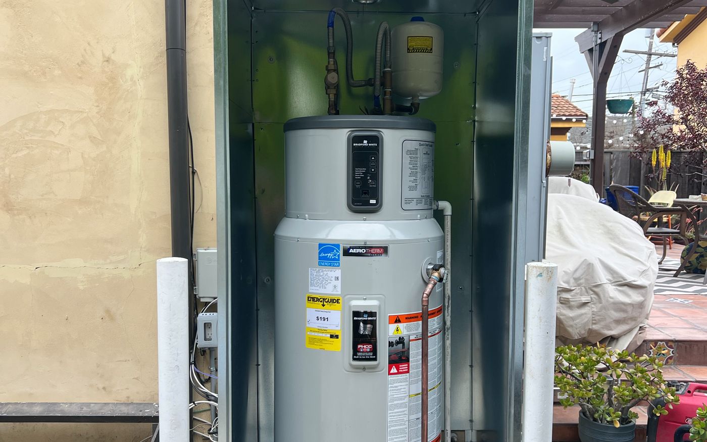 New Bradford White AeroTherm heat pump water heater installed in a galvanized enclosure against an exterior wall