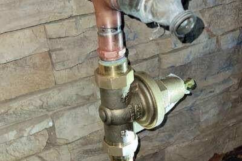New copper piping, brass pressure regulator, ball valve and hose bib installed against the same stone wall