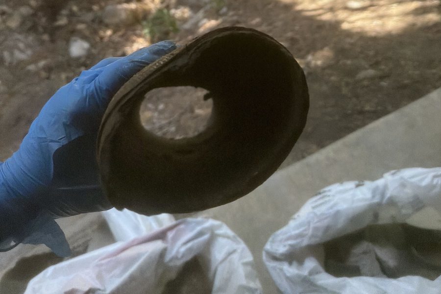 Gloved hand holding a removed section of old pipe with heavy interior buildup narrowing the opening
