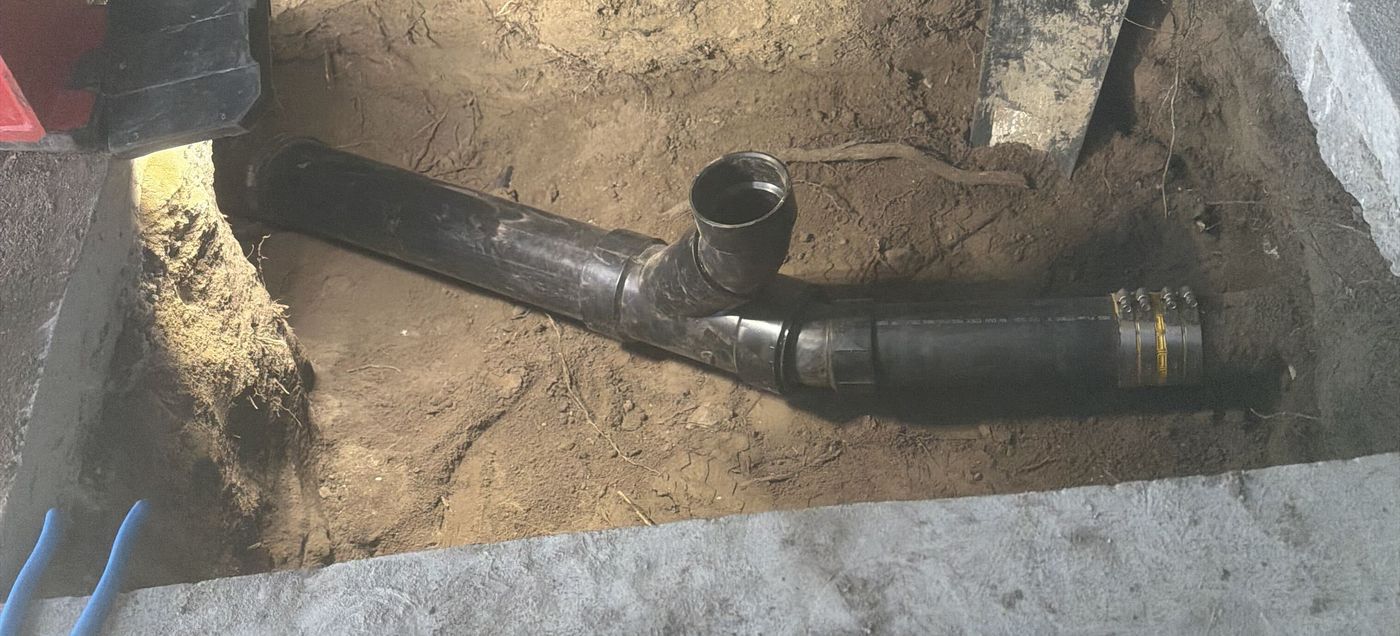 Concrete slab cut open to expose a repaired drain line, with a shovel and tools beside the pit