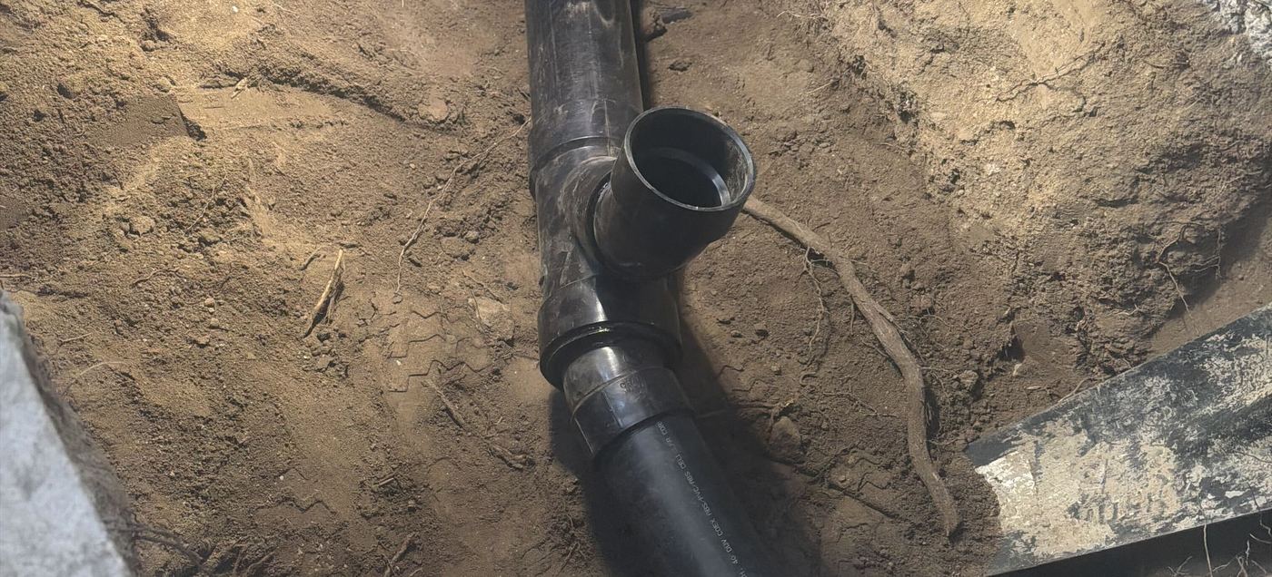 New black ABS wye fitting and riser in an open trench, joined with a banded shielded coupling